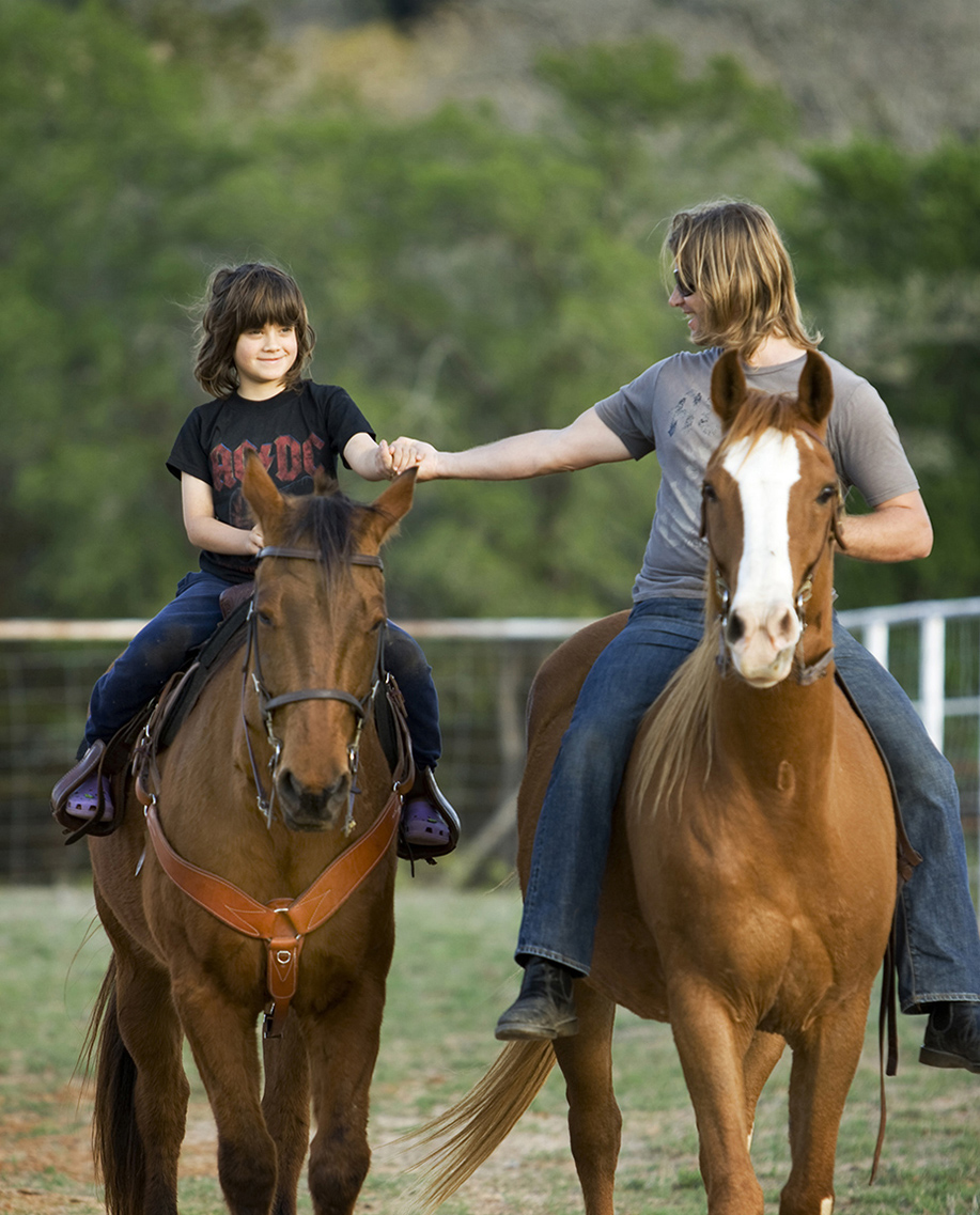 adult woman holding young boy's hand while riding horses